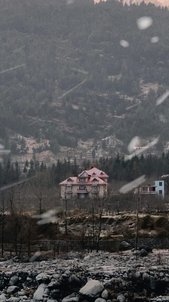 Charming pink-roofed house in the serene mountains of Manali, India, surrounded by nature.