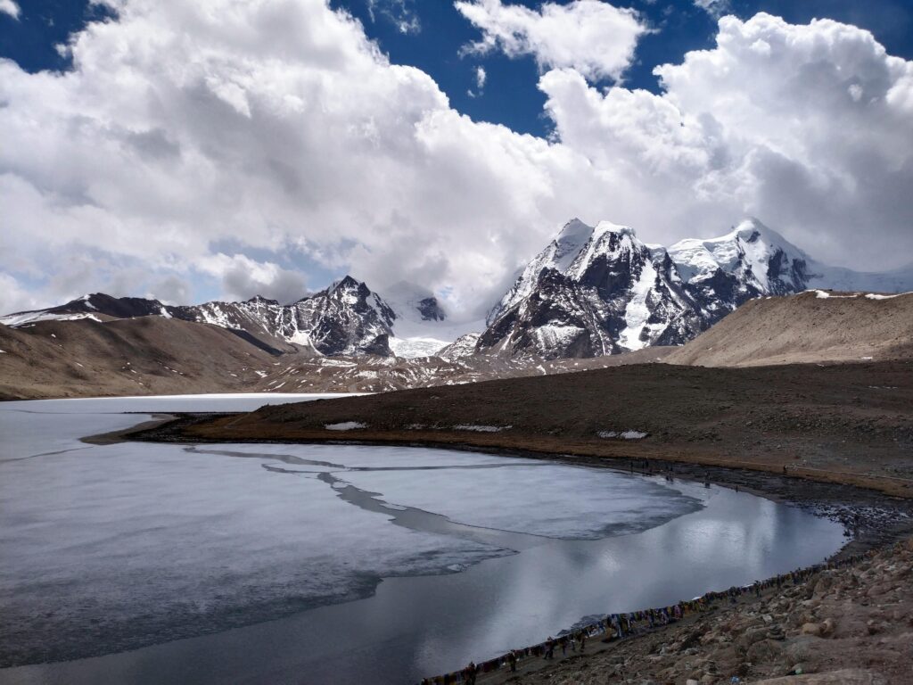 Scenic view of the snow-capped Gurudongmar Lake with mountains and clouds in Sikkim, India.