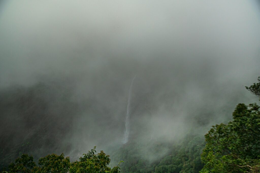 Breathtaking view of a waterfall shrouded in fog and lush greenery in Cherrapunji, India.