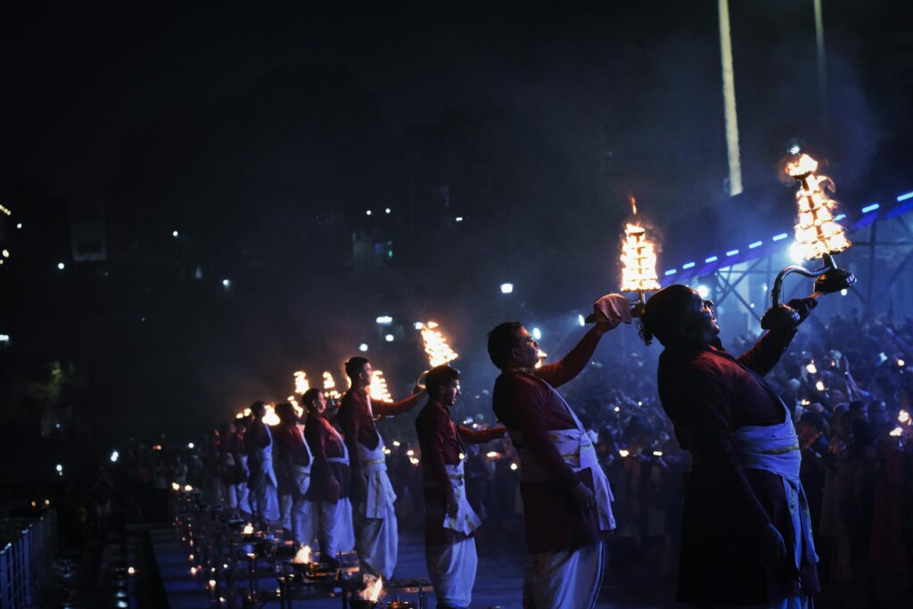 People performing a vibrant Ganga Aarti ritual at Triveni Ghat, Rishikesh, India at night.