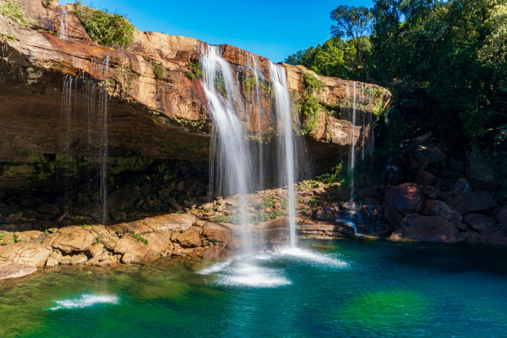 Capture of Krang Shuri Waterfall in Meghalaya, India with lush greenery and clear blue water.