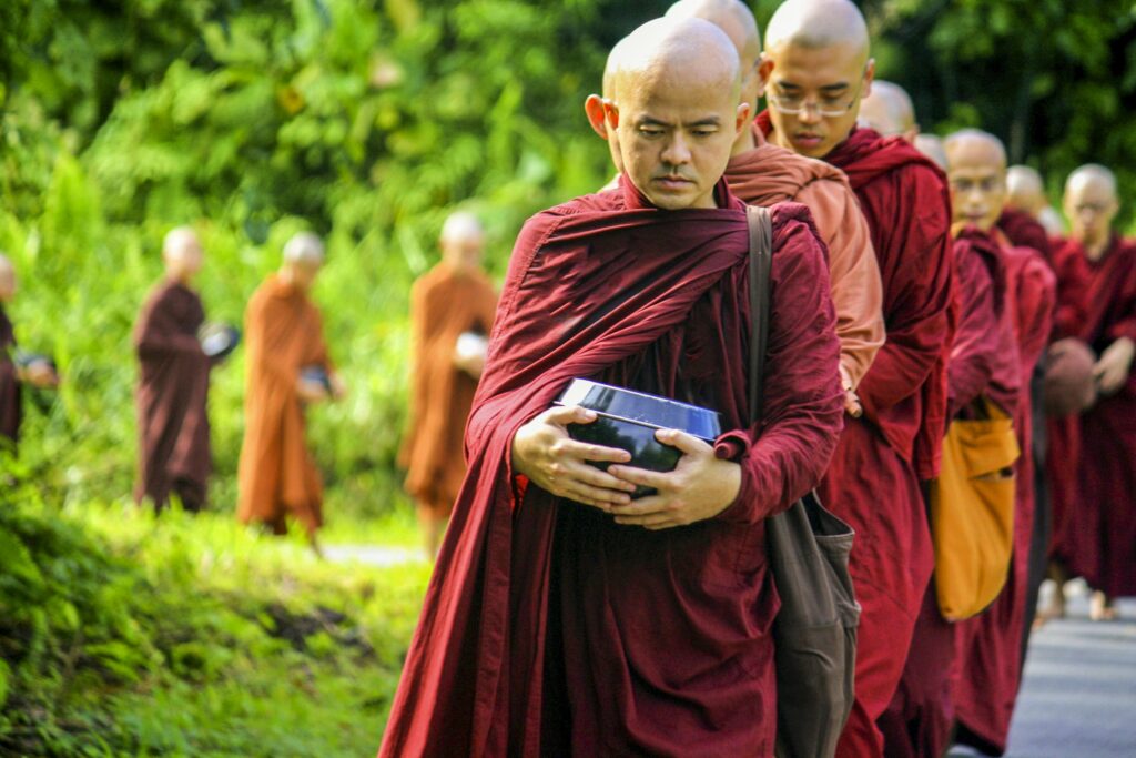 Peaceful procession of monks holding bowls in a lush green setting.