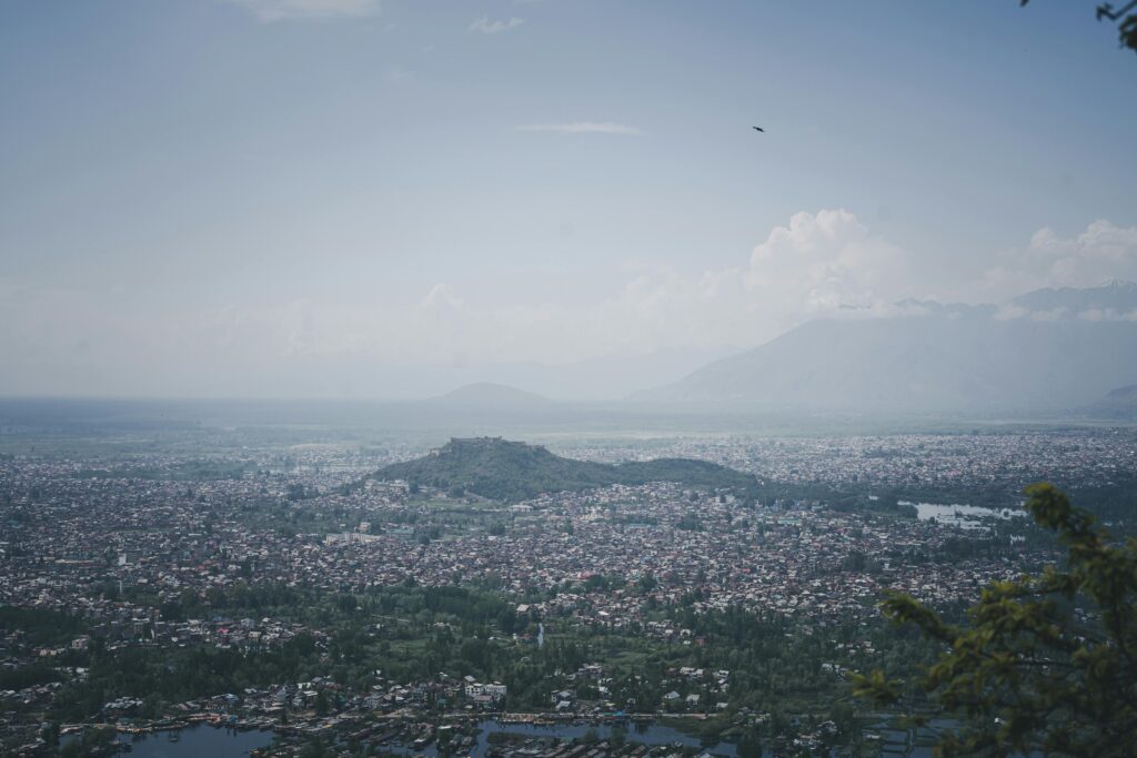 Stunning aerial shot of Srinagar cityscape with surrounding mountains under a clear blue sky.