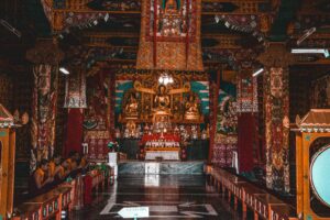 Stunning Buddhist temple interior with ornate decorations and monks in prayer, showcasing vibrant cultural and religious artistry.