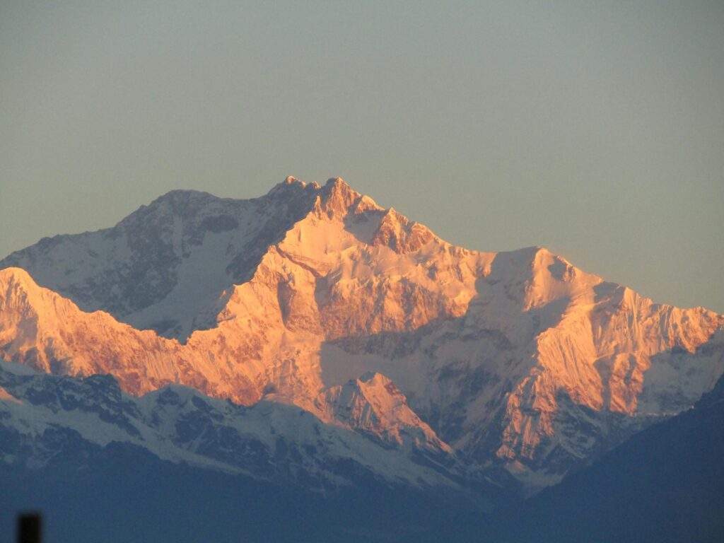 Snow-capped peaks of Kanchenjunga bathed in golden sunrise light, showcasing nature's majesty.