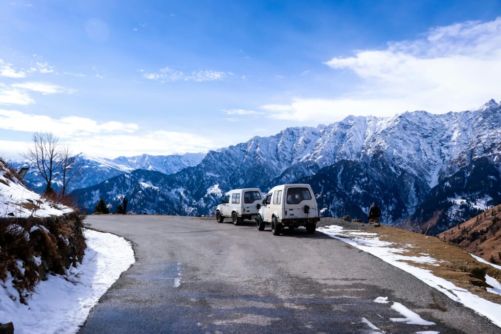 Idyllic winter road trip scene with vehicles and mountains in Himachal Pradesh.