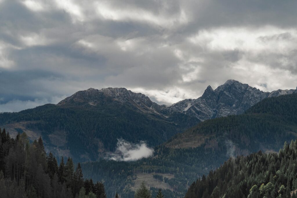 Scenic view of a dramatic mountain range with lush forest under cloudy skies.