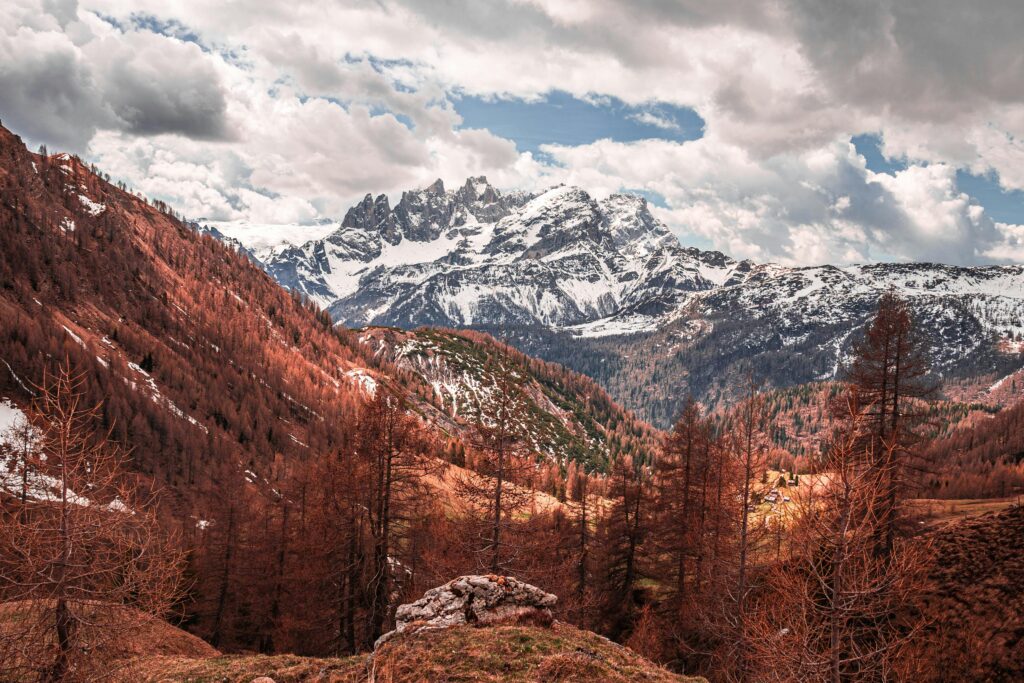 Panoramic view of Dolomite mountains with autumn foliage and snow-capped peaks.