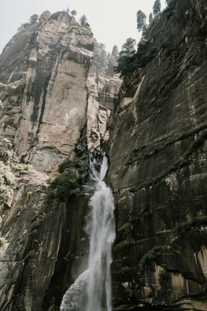 Low angle of fast Jogini Waterfall flowing among rough rocky cliff on sunny day in Manali