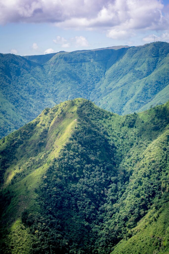 A scenic view of lush green hills in West Khasi Hills, India under a vibrant blue sky.