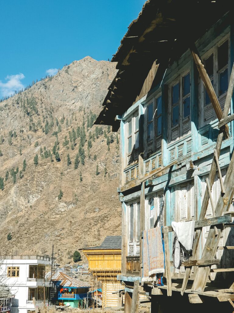 Sunlit wooden houses in Kasol, HP, India with mountain backdrop. Perfect rural scene.