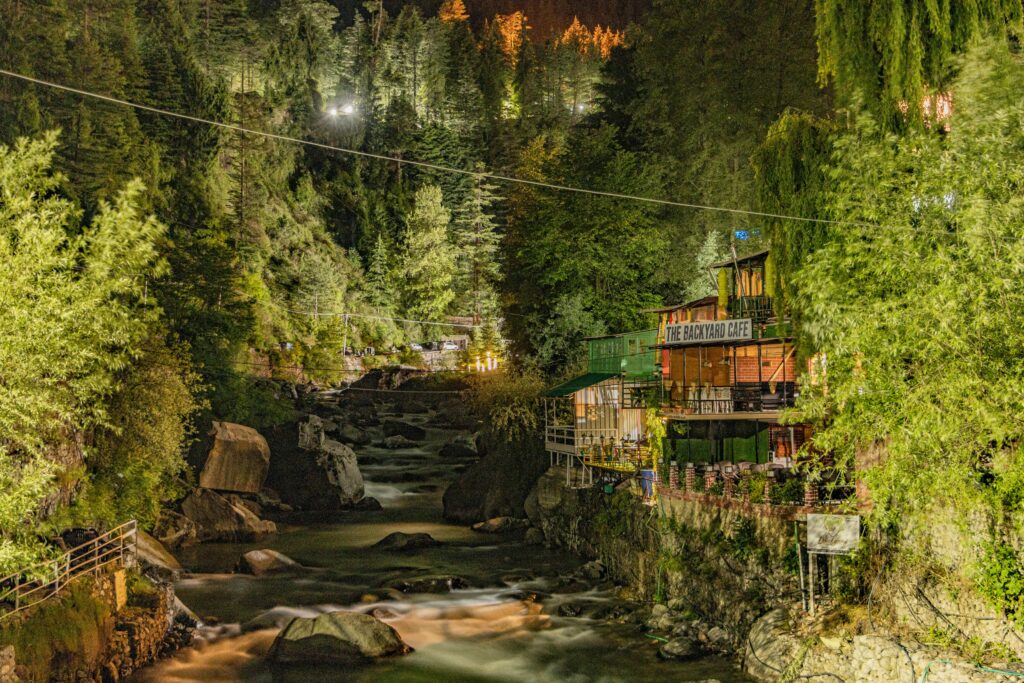 Scenic night view of river and greenery in Manali, India featuring The Backyard Cafe.