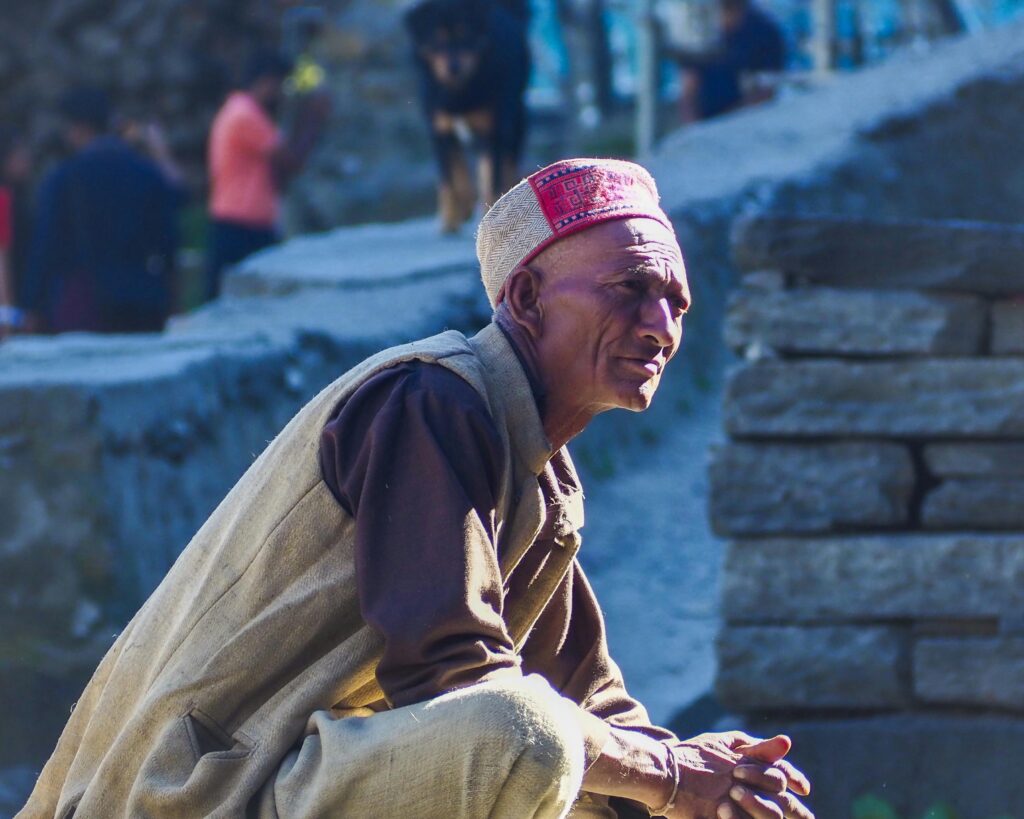 Portrait of an elderly South Asian man wearing a traditional Himachal cap, outdoors in Malana, India.