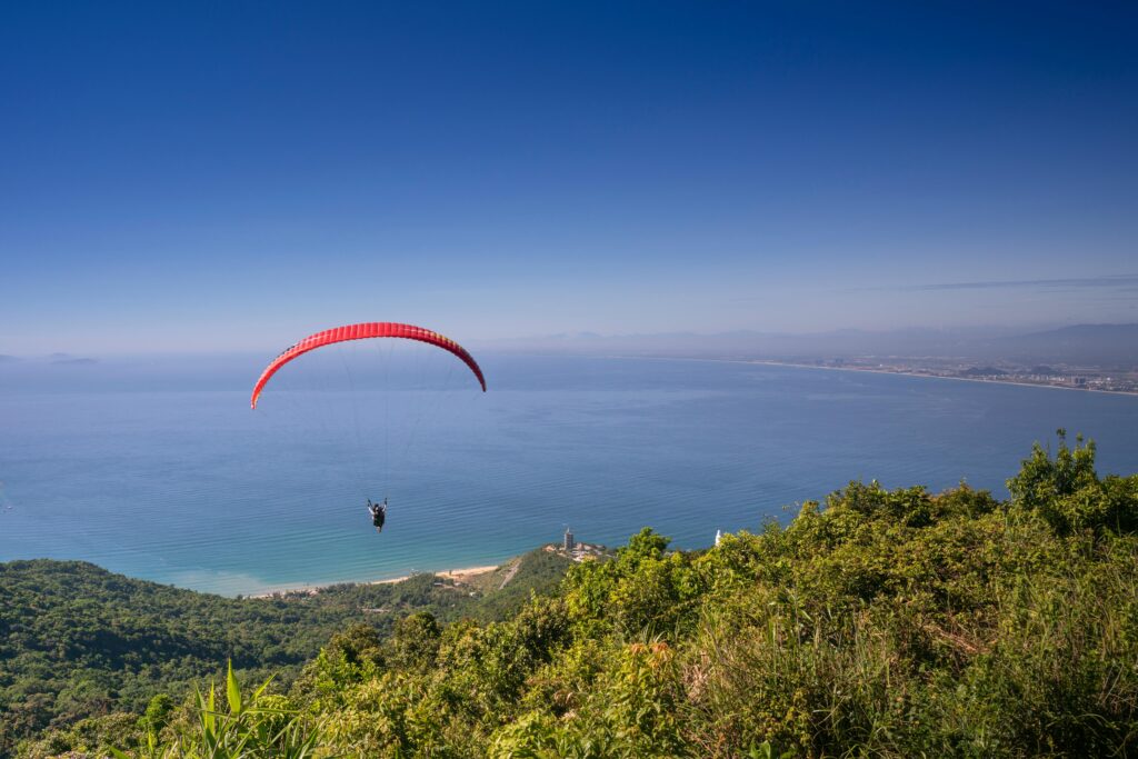 A paraglider flies over a beautiful coastal landscape with clear skies, offering a stunning view at kasol