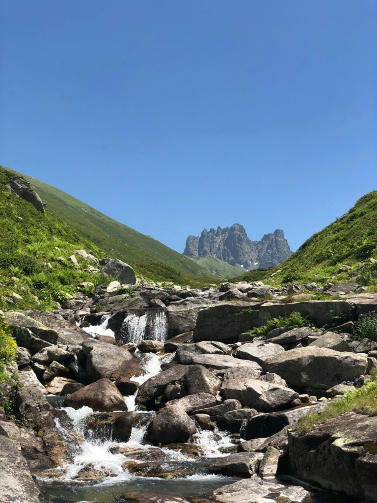 Idyllic view of a mountain stream flowing through rocky terrain under clear blue skies.