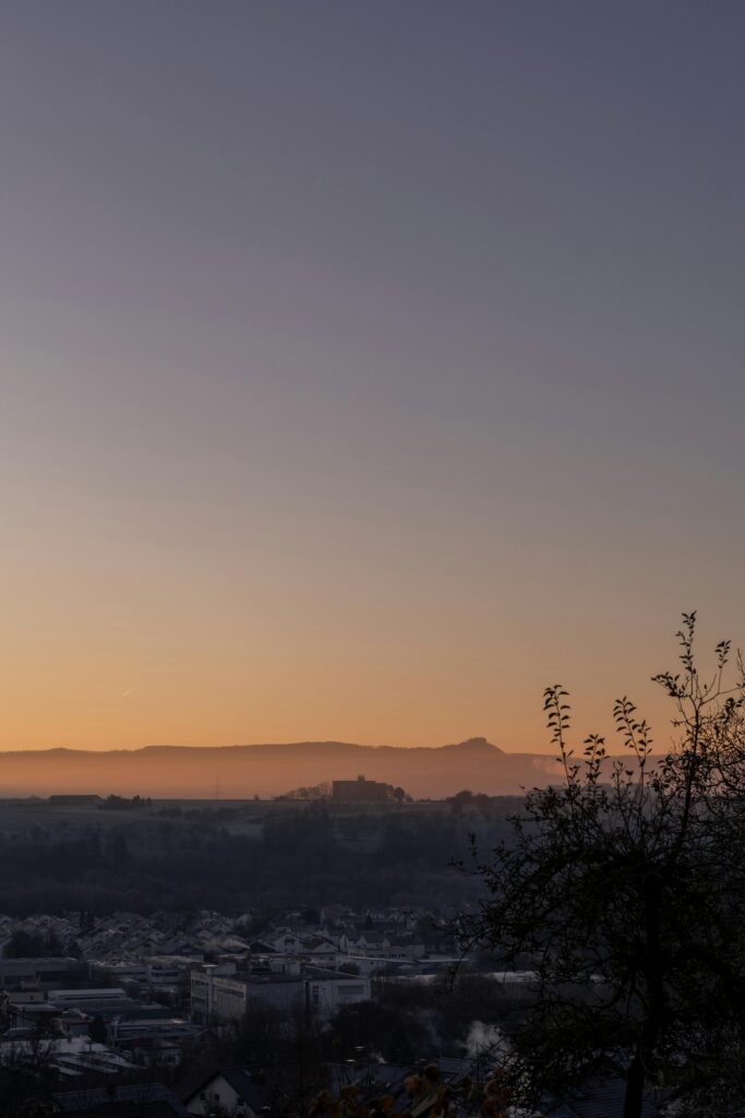 Serene sunset view over a small town with silhouette of trees and distant hills in the background.