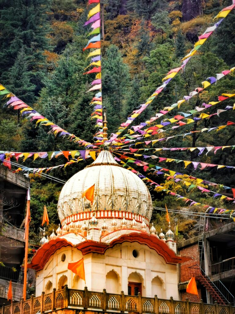 A vibrant Hindu temple in India surrounded by colorful flags and lush greenery, showcasing architectural beauty.