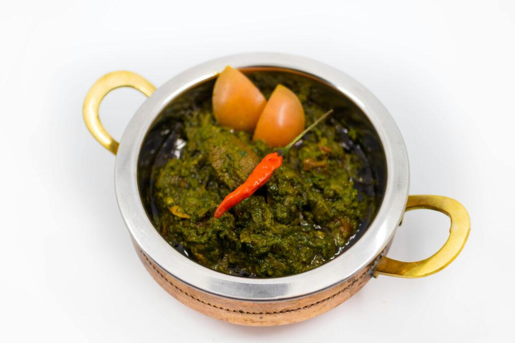 Close-up of spicy Indian saag dish garnished with chili in a traditional brass bowl.